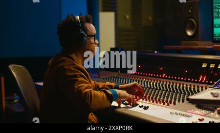 Audio designer che regola l'audio su una scrivania di controllo del mixer, concetto di studio musicale professionale. Il produttore alza il volume e aggiunge effetti su una console di mixaggio, registrando brani dal vivo. Telecamera A.. Foto Stock