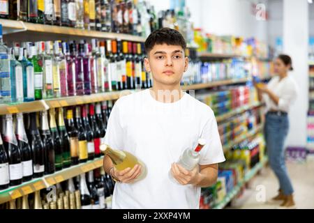 Interessato giovane ragazzo che sceglie bevande alcoliche in negozio Foto Stock