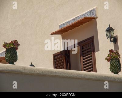 Finestra aperta con persiane rosse, piante in vaso e lampada da parete su parete beige, palermo, sicilia, mediterraneo, italia Foto Stock