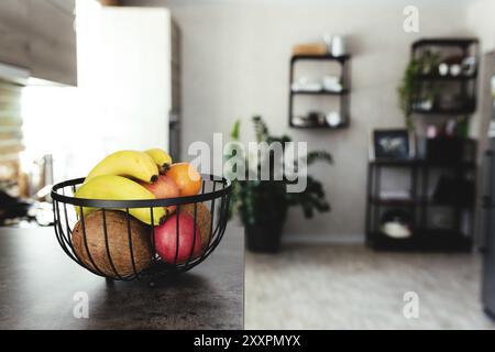 Frutti tropicali: Cocco rotto, mela, mandarino, arancia, banana in un cestino di frutta sul bancone del bar nell'elegante cucina mansardata. Sfondo sfocato. Foto Stock