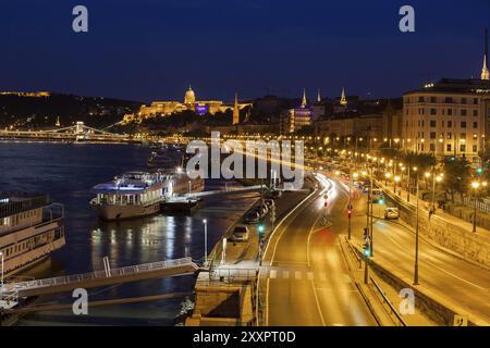 Città di Budapest di notte in Ungheria, strada e navi da crociera sul Danubio sul lato di Buda, vista verso il castello Foto Stock