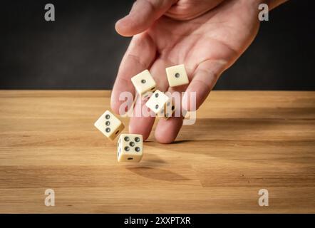 Mano che lancia cinque dadi su un tavolo di legno Foto Stock