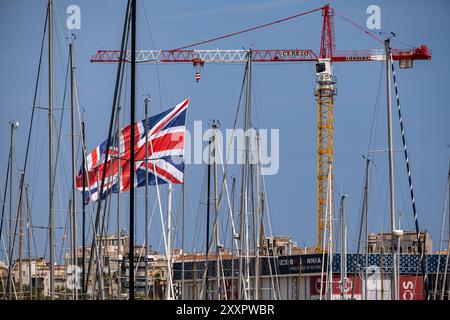 Barcellona, Spagna. 25 agosto 2024. La bandiera della squadra britannica si vede sventolare al porto di Barcellona tra alberi e barche. Si è svolta l'ultima gara preliminare della Coppa America. Molti spettatori hanno seguito la gara dal Race Village situato a Port de la Fusta, dove viene offerta anche una vasta gamma di gastronomia. Credito: SOPA Images Limited/Alamy Live News Foto Stock