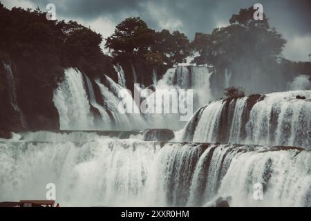 Le potenti cascate scorrono su aspre scogliere, circondate da vegetazione lussureggiante e nebbia sotto un cielo spettacolare e nuvoloso. Foto Stock