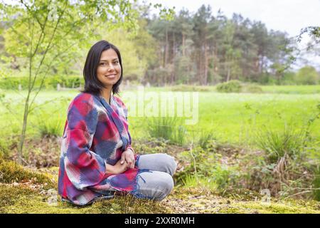 Giovanissimo colombiano donna seduta nel bosco in prossimità di pascolo verde Foto Stock