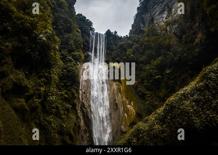 Un'alta cascata si tuffa lungo una ripida e lussureggiante scogliera circondata da fitte fogliame e rocce coperte di muschio, creando un suggestivo paesaggio naturale Foto Stock