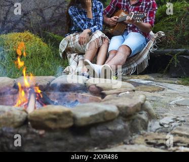 Coppia giovane con la chitarra vicino a fuoco all'aperto. Viaggi e vacanze concept Foto Stock