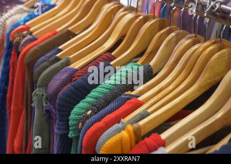 Vari capi colorati splendidamente disposti su appendiabiti in legno all'interno di un negozio boutique Foto Stock