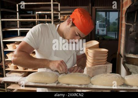 Giovane panettiere che segna la parte superiore di pane lievito madre non cotto con una lama di rasoio presso il forno a legna Flour Salt + Water nella città di Berry, nel nuovo Galles del Sud, in Australia Foto Stock