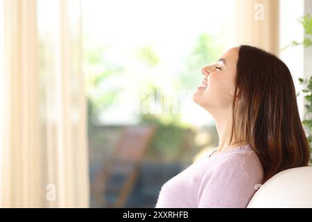 Vista laterale ritratto di una donna felice che respira aria fresca seduta su un divano in una casa di lusso Foto Stock