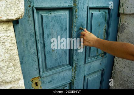 Uomo in procinto di entrare in un edificio - foto ravvicinata di una mano di un uomo che tiene la maniglia al centro di una bellissima porta di legno blu. Foto Stock