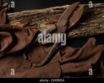 Vecchie forbici sartoriali arrugginite su legno invecchiato con tessuto marrone Foto Stock