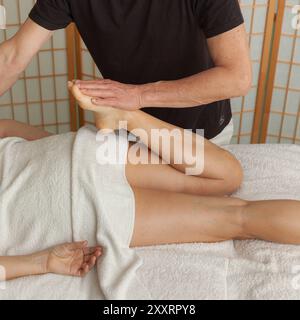 Il terapeuta esegue la regolazione delle gambe sul client durante la sessione chiropratica. La terapia manuale favorisce la mobilità, il recupero e l'alleviamento del dolore. Foto Stock