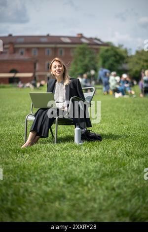 Donna d'affari sicura e felice con gli auricolari, utilizza un computer portatile, lavora in un parco verde con la sola poltrona Foto Stock