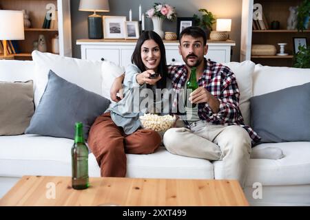 Una coppia seria guarda la TV insieme mentre si siede su un divano nel soggiorno. Fidanzata e fidanzato abbracciano, coccolano, parlano e guardano la TV St Foto Stock