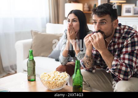 Una coppia seria guarda la TV insieme mentre si siede su un divano nel soggiorno. Fidanzata e fidanzato abbracciano, coccolano, parlano e guardano la TV St Foto Stock