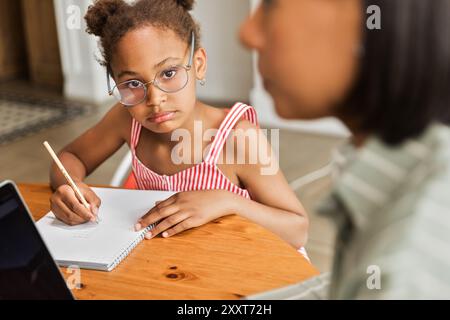 Ritratto ragazza afroamericana che fa i compiti vicino a una madre che lavora Foto Stock