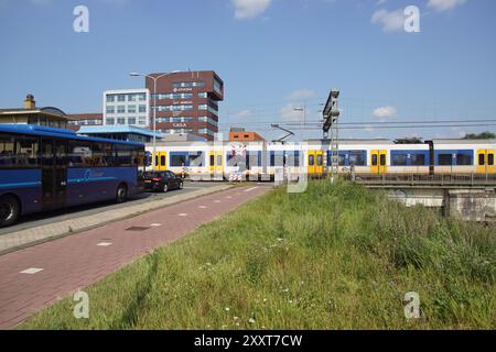 Alkmaar, Paesi Bassi, 25 agosto 2024. Passaggio a livello con un treno di passaggio e in attesa dell'autobus Qliner e auto nella città olandese di Alkmaar. Foto Stock