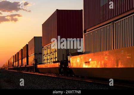 Il bagliore rosso del tramonto su un treno di container impilati di passaggio Foto Stock