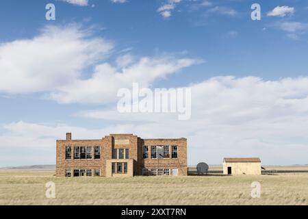 Un edificio scolastico abbandonato in un campo Foto Stock