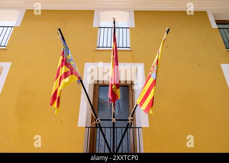 Foto di una selezione di 3 bandiere spagnole su un edificio giallo nella città di Villajoyosa ad Alicante in Spagna che mostra la Comunità spagnola e valenciana Foto Stock