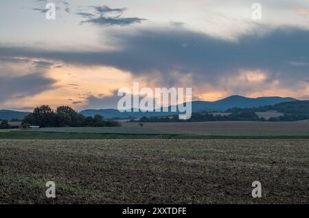 Paesaggio rurale con campo arato, splendido cielo arancione e nuvole fumose al tramonto. Superficie agricola. Chocholna, Slovacchia Foto Stock