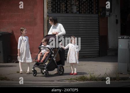 Una madre ebrea ortodossa di 3 pause per parlare con le sue ragazze, 2 delle quali indossano gli stessi vestiti. A Brooklyn, New York, 2024. Foto Stock