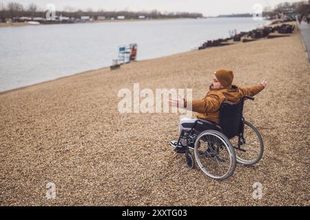 Immagine della vista posteriore dell'uomo paraplegico portatore di handicap in sedia a rotelle sul lago. Si sta divertendo all'aperto. Foto Stock