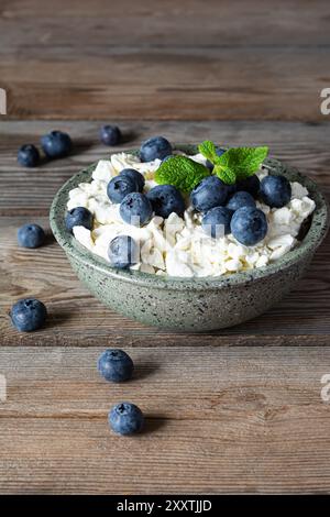 Una ciotola con formaggio fresco, yogurt, frutti di bosco freschi (mirtilli) e menta fresca su fondo di legno. Colazione deliziosa, cibo sano. Foto Stock