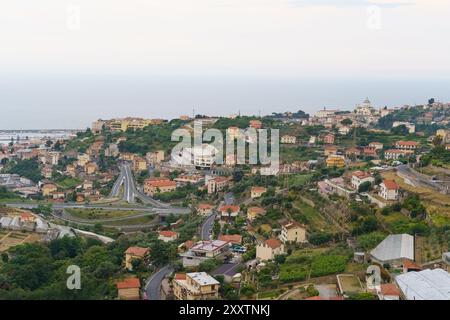 Un'immensa cittadina costiera in Italia, incastonata tra verdi colline, con strade tortuose e una vasta distesa di mare in lontananza. Foto Stock