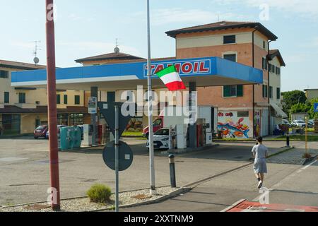 Rovato, Italia - 8 giugno 2023: Un uomo cammina dall'altra parte della strada di fronte a un distributore di benzina in Italia. Il distributore di benzina ha una tettoia blu e la bandiera italiana Foto Stock