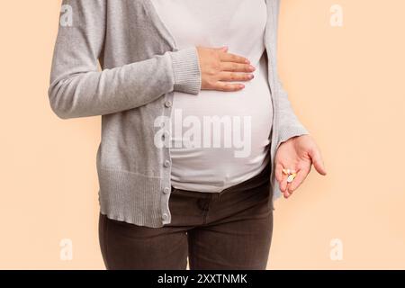 Irriconoscibile la donna incinta che mostra pillole toccando pancia in studio, ritagliato Foto Stock