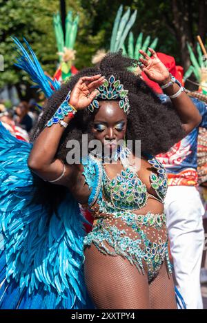 Notting Hill, Londra, Regno Unito. 26 agosto 2024. Il più grande festival di strada d'Europa si svolge nelle strade di Notting Hill. Ballerini esotici a tema giamaicano e gruppi musicali sfilano per le strade, con cibo e intrattenimento di strada intorno alla zona che si aggiungono all'evento. La Grand Parade si svolge il lunedì festivo come il culmine del festival di tre giorni, iniziato nel 1966. Ballerina che si esibisce Foto Stock