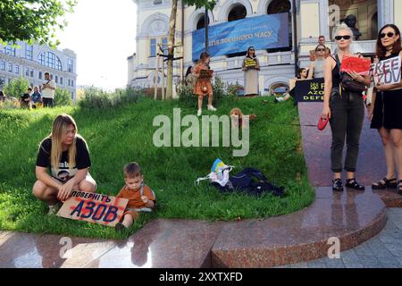 KIEV, UCRAINA - 25 AGOSTO 2024 - Una donna e un bambino siedono sul prato fuori dal Taras Shevchenko National Academic Opera and Ballet Theatre durante il Don't Be Silent! La prigionia uccide raduno tenuto per ricordare il personale militare nella prigionia russa, Kiev, capitale dell'Ucraina. Foto Stock