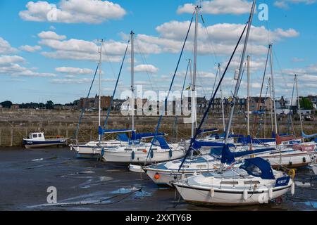 EDIMBURGO - 28 LUGLIO 2024: Le barche a vela sono ormeggiate pacificamente nel porto di Fisherrow, circondato da un tranquillo corso d'acqua e da un cielo blu brillante. Foto Stock