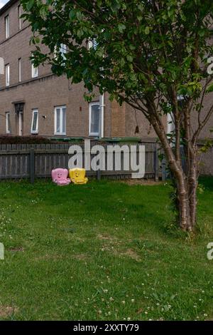 EDIMBURGO - 28 LUGLIO 2024: Sedie di colore rosa e giallo si trovano sull'erba in un cortile accanto a un edificio residenziale a Fisherrow. Foto Stock