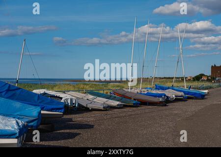 EDIMBURGO - 28 LUGLIO 2024: Barche a vela colorate riposano sulla riva di Fisherrow sotto un cielo blu luminoso con soffici nuvole, offrendo una vista serena. Foto Stock