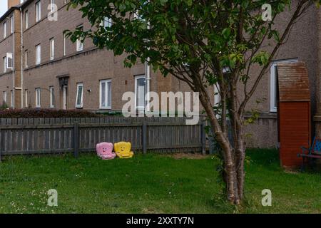 EDIMBURGO - 28 LUGLIO 2024: Due luminose sedie di plastica si siedono sull'erba accanto a un edificio residenziale a Fisherrow in una giornata di sole, Foto Stock