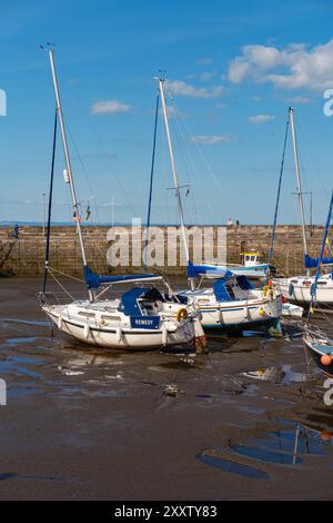 EDIMBURGO - 28 LUGLIO 2024: Le barche a vela sono ancorate e riposano sul fango mentre la marea si ritira, rivelando la costa del porto di Fisherrow sotto il cielo luminoso. Foto Stock