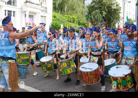 Londra, Regno Unito. 26 agosto 2024. Le persone che si godono il carnevale oggi, a Londra, nel Regno Unito, ma con la tensione dopo le pugnalate di ieri, lasciando tre persone in ospedale. Qui, la musica del Tribo, ispirata alle tribù indigene amazzoniche, i batteristi del Tribo mostreranno autentici ritmi di samba reggae che hanno avuto origine dal movimento dell'orgoglio nero nella città di Salvador de Bahia, intorno al 1969. Crediti: Mary-Lu Bakker/Alamy Live News Foto Stock