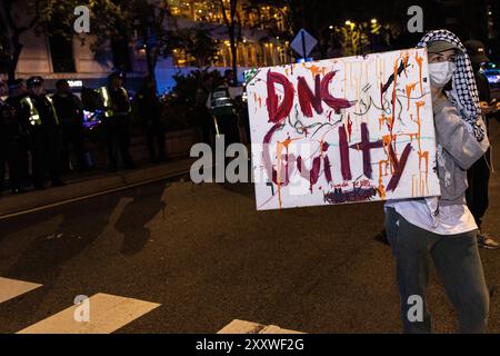 Chicago, Stati Uniti. 22 agosto 2024. Un attivista pro-Palestina ha un cartello che recita "DNC Guilty" durante una manifestazione di rumore nei pressi dell'Omni Chicago Hotel a Chicago, Illinois, giovedì 22 agosto 2024. Gli attivisti inizialmente volevano protestare vicino al Park Hyatt, dove il vicepresidente Kamala Harris soggiornava prima che accettasse la nomina del Partito Democratico più tardi quel giorno, ma decisero di non farlo a causa della pesante presenza della polizia. Gli agenti di polizia di Chicago con mangoni hanno rapidamente mandato via la folla minacciando di arrestare attivisti e giornalisti. Crediti: SIPA USA/Alamy Live News Foto Stock