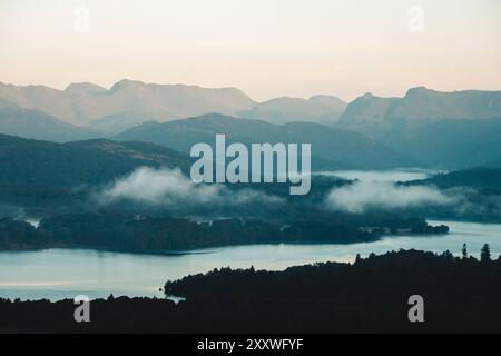 Una splendida vista mattutina attraverso Windermere fino alle spettacolari Langdale Pikes nel Lake District, presa dal punto panoramico di Orrest Head dopo l'alba. Foto Stock