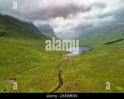 Splendida prospettiva aerea che mostra il tranquillo lago annidato tra le vibranti colline verdi e le montagne nelle mozzafiato Highlands scozzesi. Foto Stock