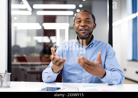 Uomo professionista sicuro di sé in camicia blu che partecipa a discussioni animate durante le riunioni in un ufficio moderno. I gesti espressivi aggiungono dinamismo alla conversazione Foto Stock