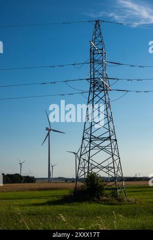 Turbine eoliche e piloni elettrici ad alta tensione contro il cielo blu. Il sole splende dietro le turbine Foto Stock