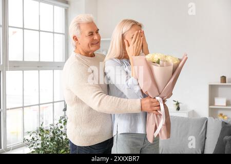 Un uomo maturo saluta sua moglie con un bouquet di rose a casa Foto Stock