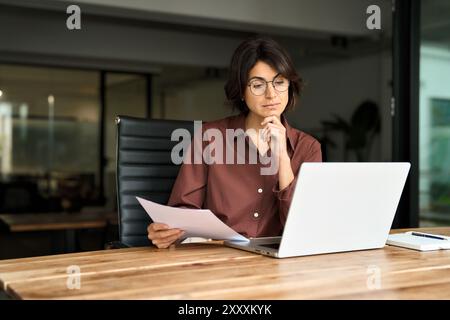 Giovane donna d'affari impegnata che lavora su un notebook che controlla i documenti. Foto Stock