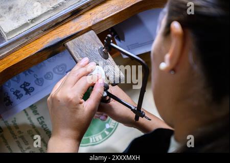 Gioielliera che taglia un oggetto metallico con una sega nella sua officina Foto Stock