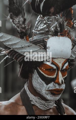 Guerriero delle Highlands della Papua nuova Guinea, con il volto decorato con colori audaci, un grande copricapo piumato, lancia in mano e calci ferocemente. Foto Stock