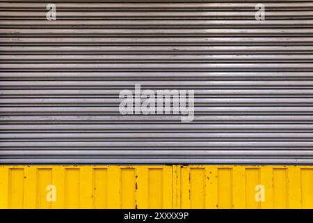 Garage in metallo ondulato orizzontale vecchio e resistente agli agenti atmosferici e porta del negozio con un bordo giallo Foto Stock
